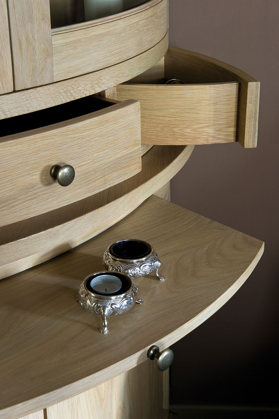 Helles Holz-Sideboard mit geöffneten Schubladen und zwei silbernen dekorativen Teelichthaltern auf der Oberfläche