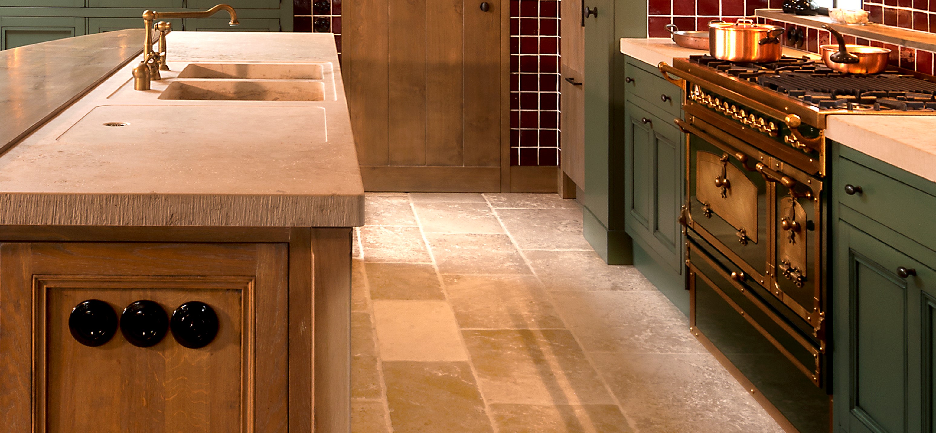Detailansicht einer eleganten Landhausküche mit Naturstein-Arbeitsplatte, goldfarbenem Gasherd, Spülbecken und grün lackierten Holzfronten
