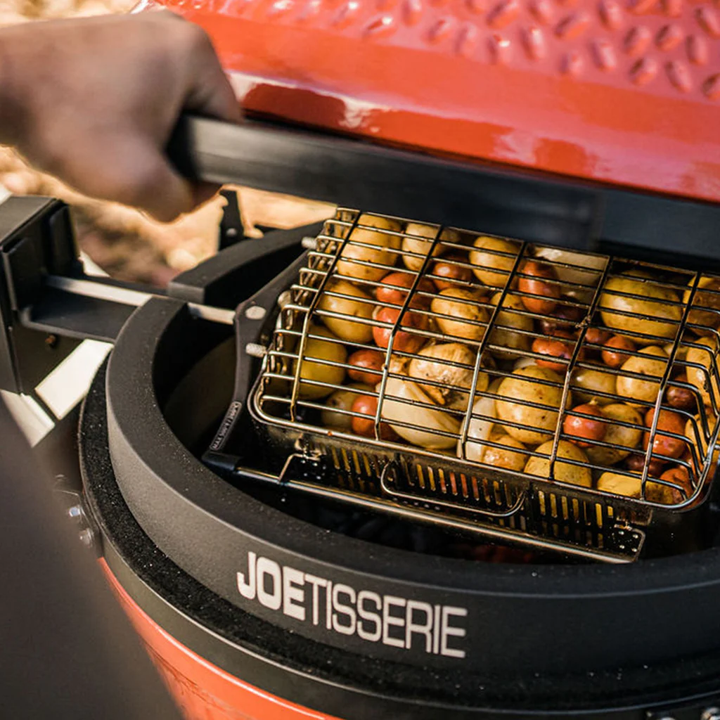 Nahaufnahme eines roten Joetisserie Grills mit geöffnetem Deckel; im Grillkorb befinden sich viele kleine Kartoffeln und Gemüse, bereit zum Grillen