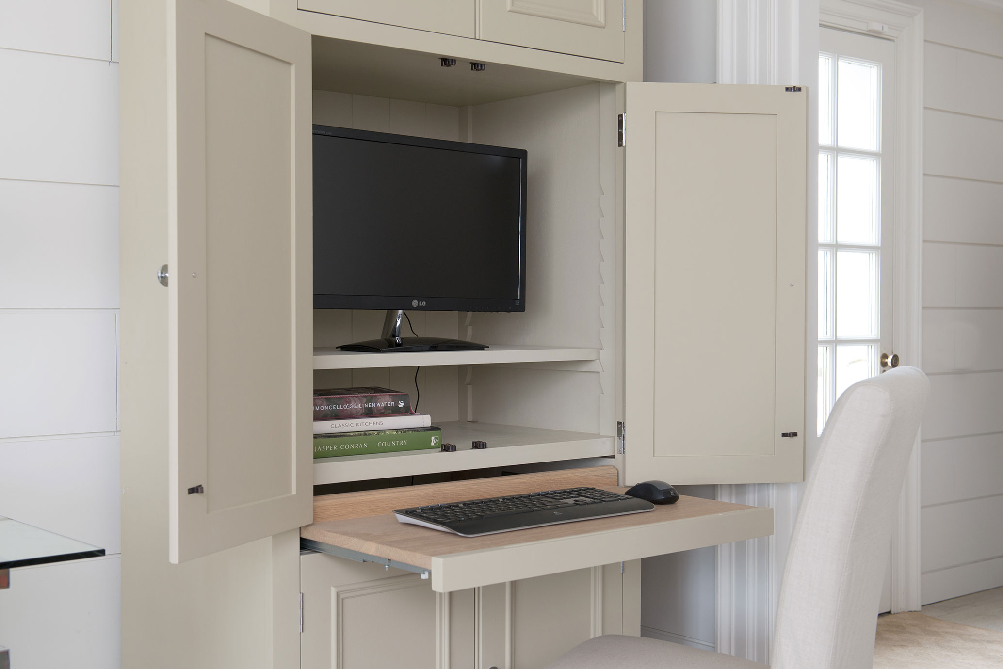 Ein beige Schrank mit geöffneten Türen, integriertem Schreibtisch, Monitor, Tastatur, Maus und Büchern, ideal für Home-Office.