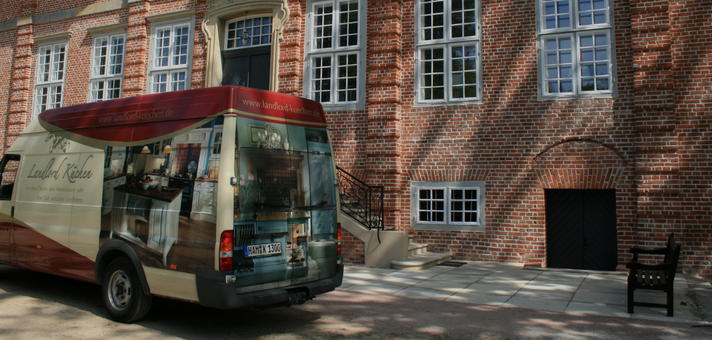 Ein Lieferwagen von Landhof-Küchen steht vor einem historischen Gebäude aus rotem Backstein mit weißen Fenstern und einer schwarzen Tür.
