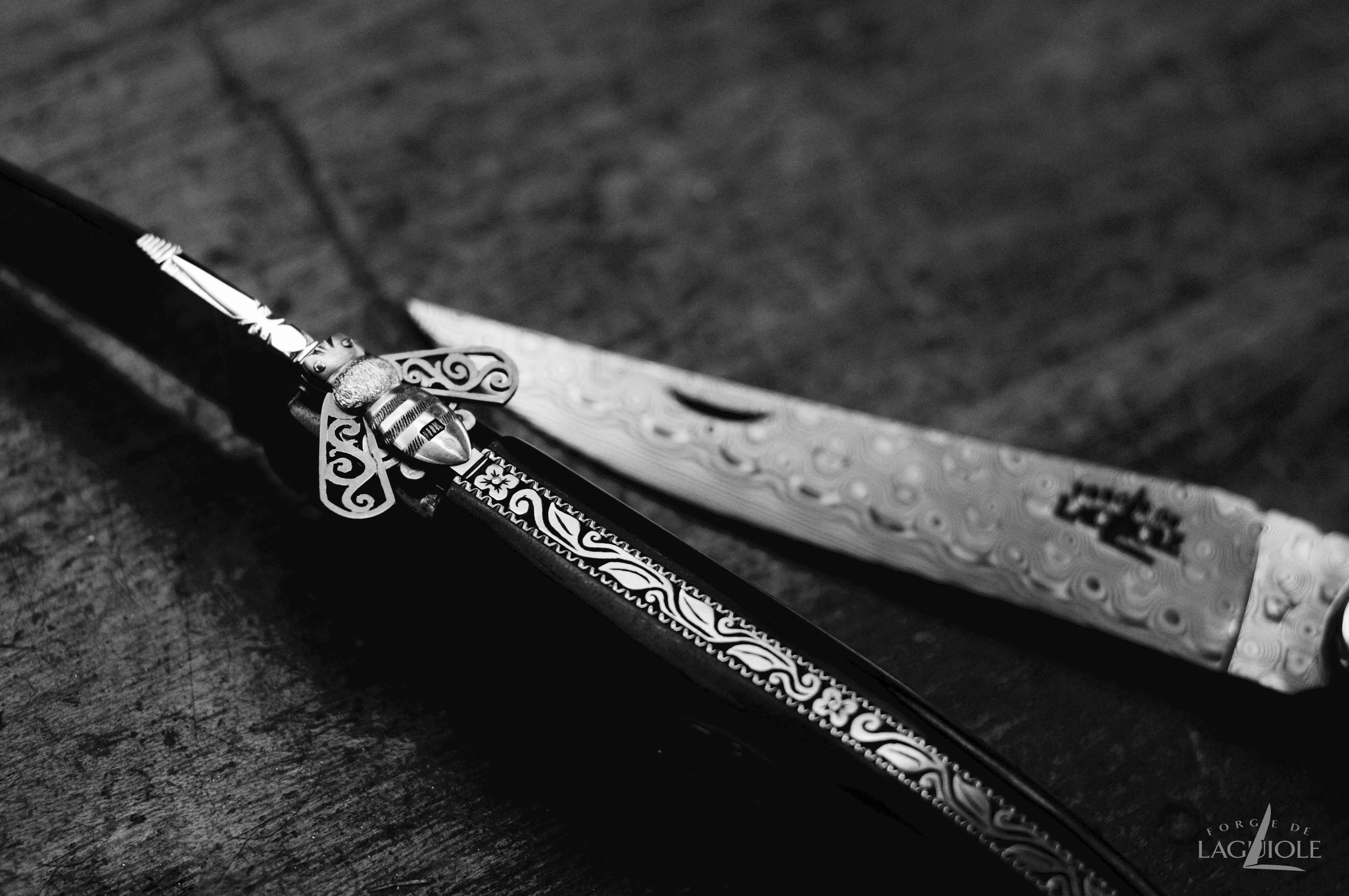 Nahaufnahme eines handgefertigten Laguiole Messers aus Damaststahl mit kunstvoller Verzierung und charakteristischer Biene auf dem Griff