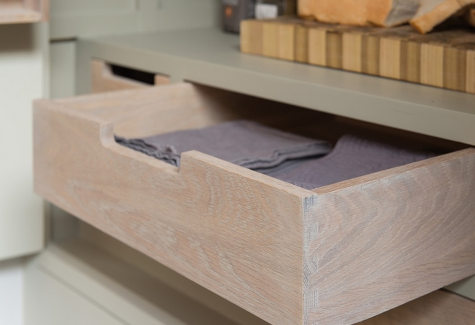 Detailaufnahme einer offenen Holz-Schublade mit ordentlich gefalteten grauen Stoffservietten in einer modernen Kücheneinrichtung