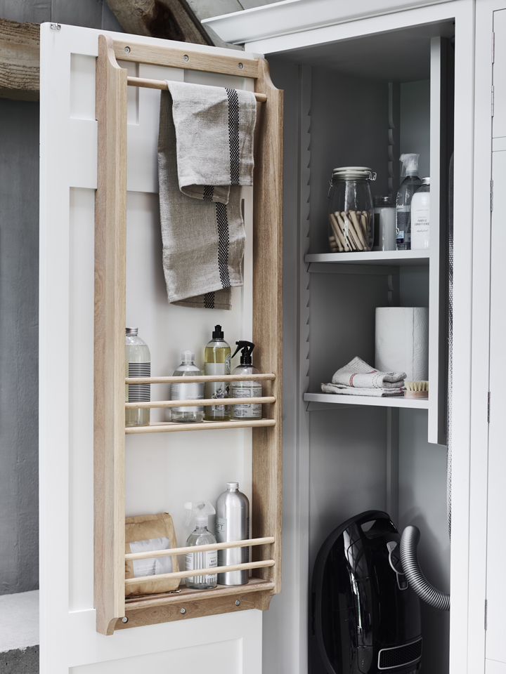 Offener Küchenschrank mit Holzregal an der Tür, Handtuchhalter, Reinigungsmittel, Sprühflasche und Utensilien, sowie Staubsauger und weitere Putzutensilien im Inneren