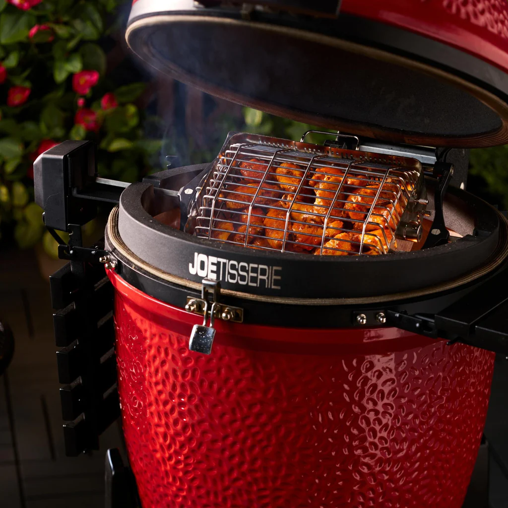 Roter Kamado Joe Grill mit geöffnetem Deckel, JoeTisserie Rotisserie und grillenden Hähnchenflügeln