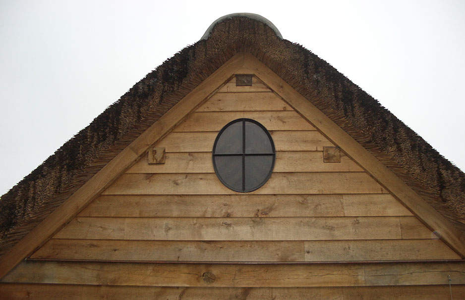 Detailaufnahme der Giebelseite eines Hauses mit natürlicher Holzverschalung, Reetdach und rundem Fenster