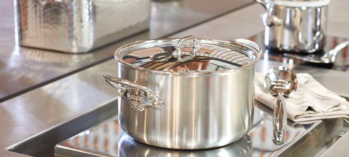 Glänzender Edelstahl Kochtopf mit Deckel und Griffen auf einem Herd, daneben Kochlöffel und Tuch, ideal für moderne Küchen