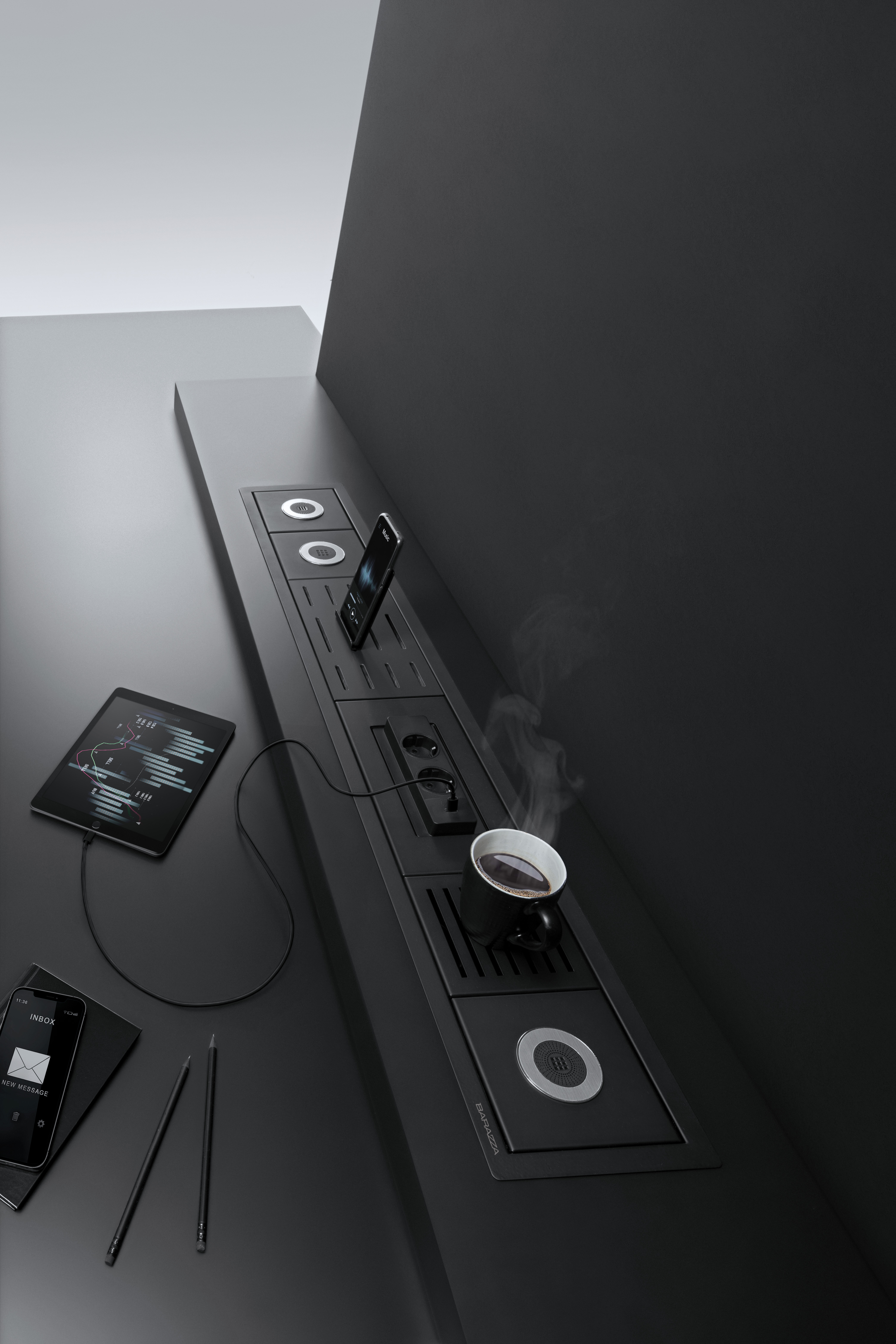 Modernes Küchensystem mit integriertem Induktionskochfeld, Steckdosen, einer Tasse Kaffee, Smartphone und Tablet auf dunkelgrauer Arbeitsfläche