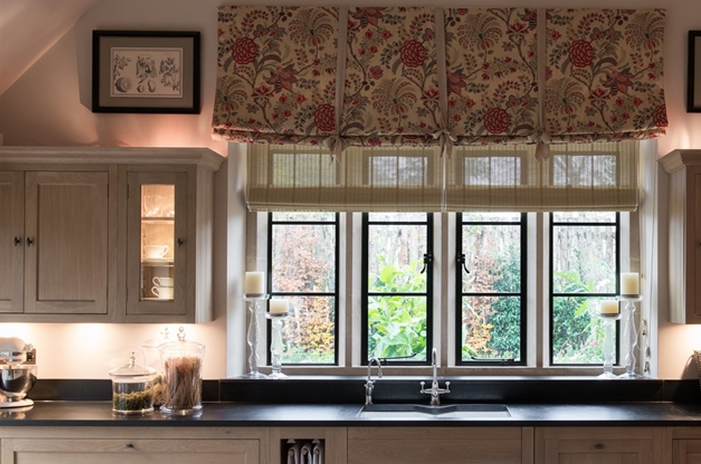 Gemütliche Küche mit großem Fenster, floralen Vorhängen, Holzschränken und dekorierten Regalen