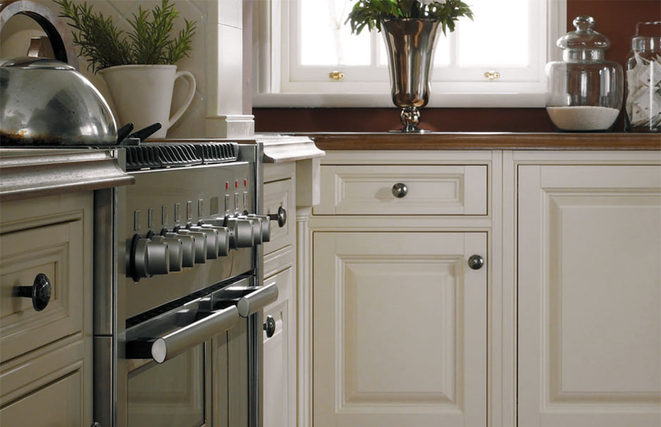Detailaufnahme einer eleganten Landhausküche mit cremefarbenen Küchenfronten, Edelstahlherd, Teekanne und Dekoration auf der Arbeitsplatte