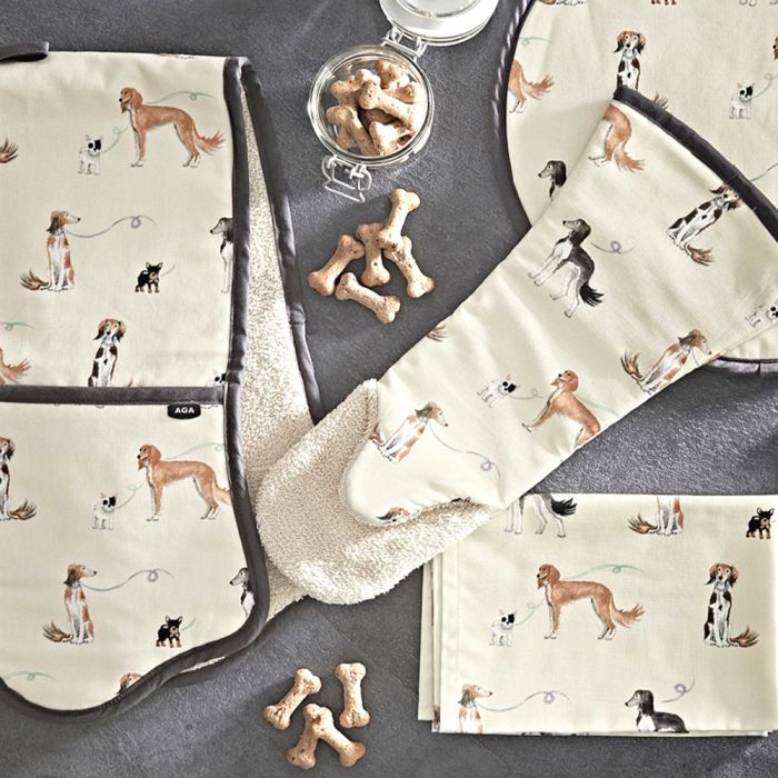 Mehrere Küchentextilien wie Topflappen, Ofenhandschuh und Platzset mit niedlichen Hundemotiven, daneben Glas und Streu von Hundekeksen