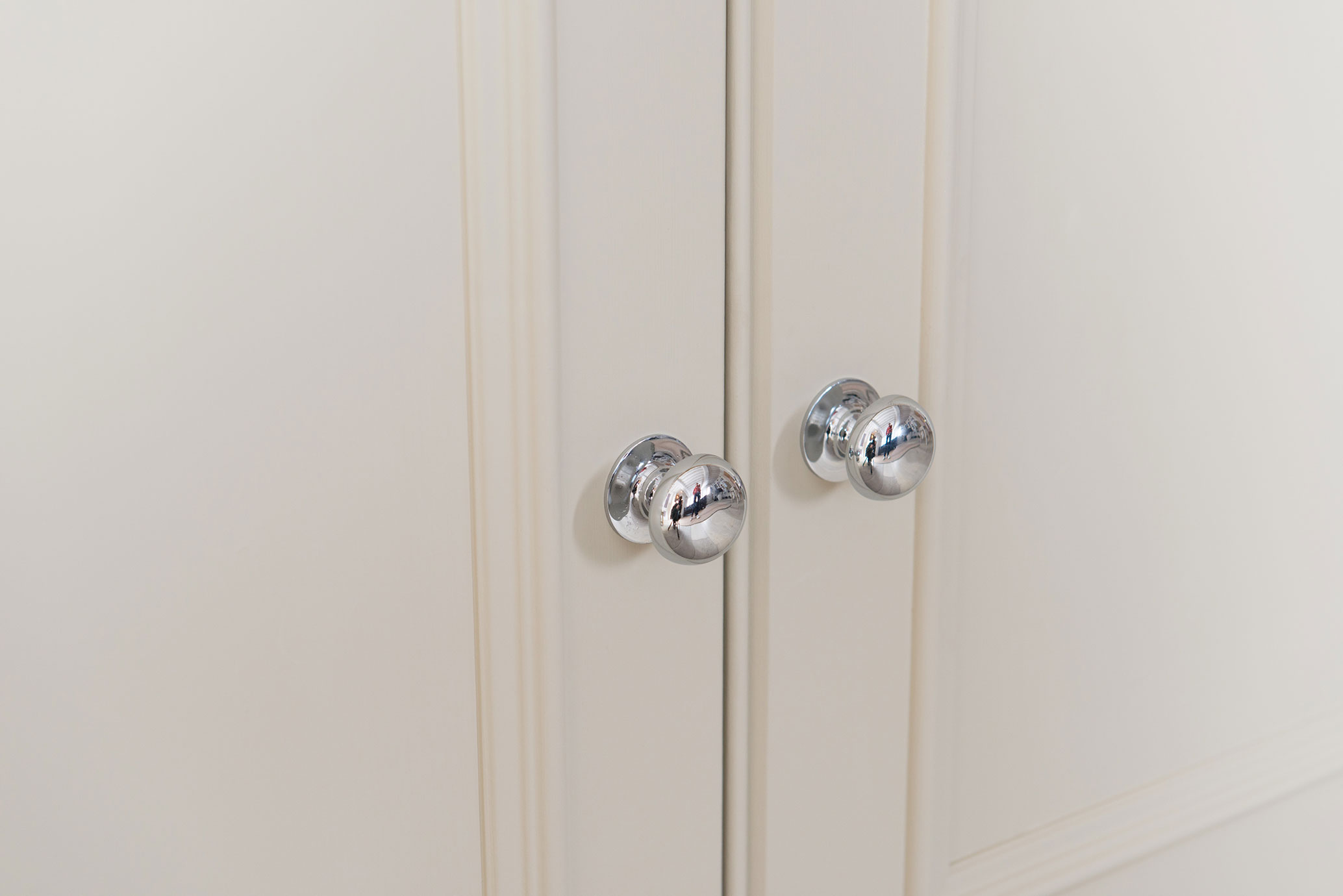 Detailaufnahme von zwei silbernen Chrom-Knaufgriffen auf einer weißen Schranktür