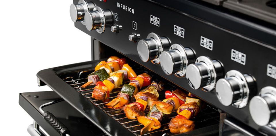 Nahaufnahme eines modernen Gasherds, auf dessen Backofengrill farbenfrohe Gemüsespieße mit Paprika, Zucchini, Zwiebeln und Fleisch liegen