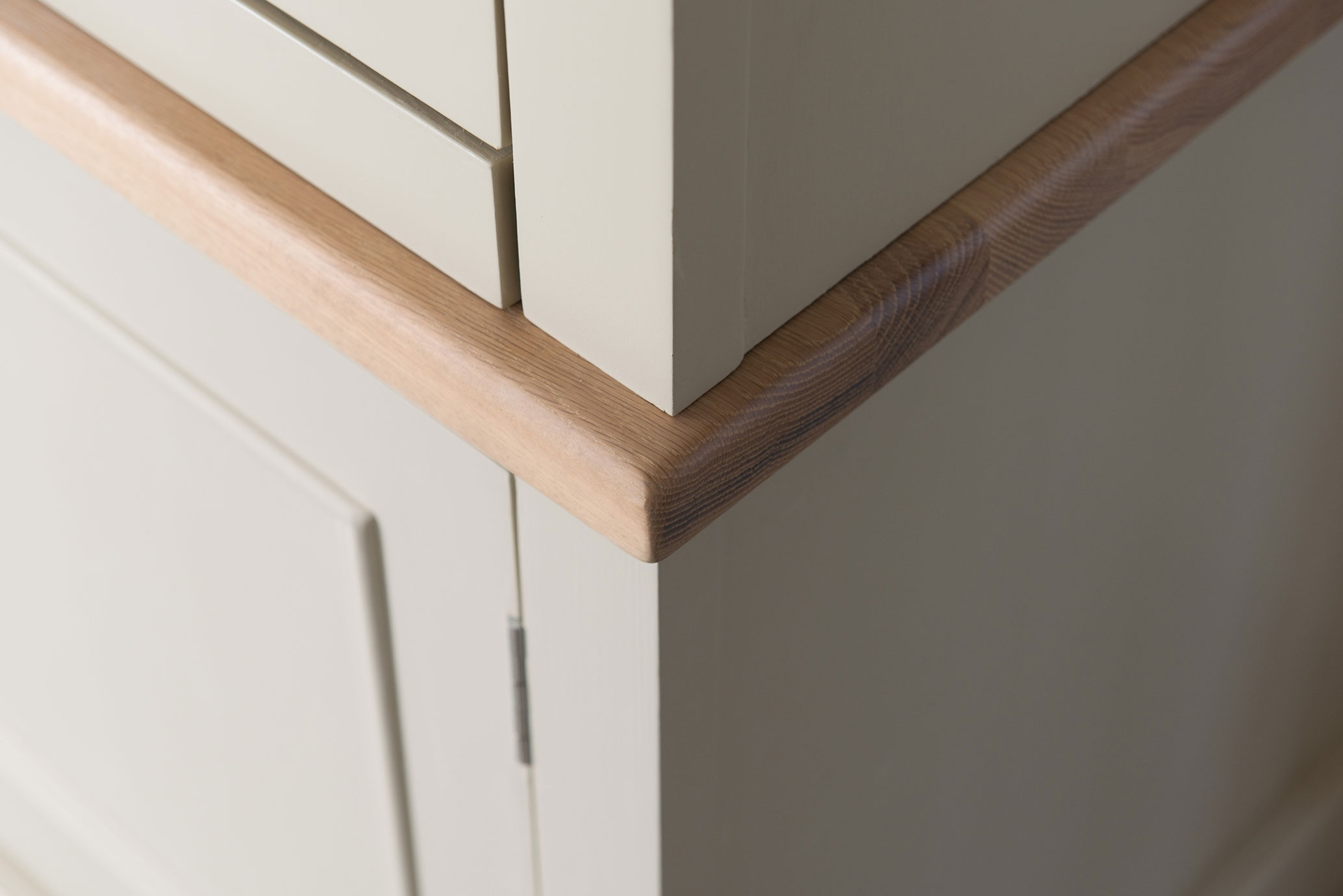 Detailfoto einer Küchenecke aus lackiertem Holz mit abgerundeter, naturbelassener Holzleiste
