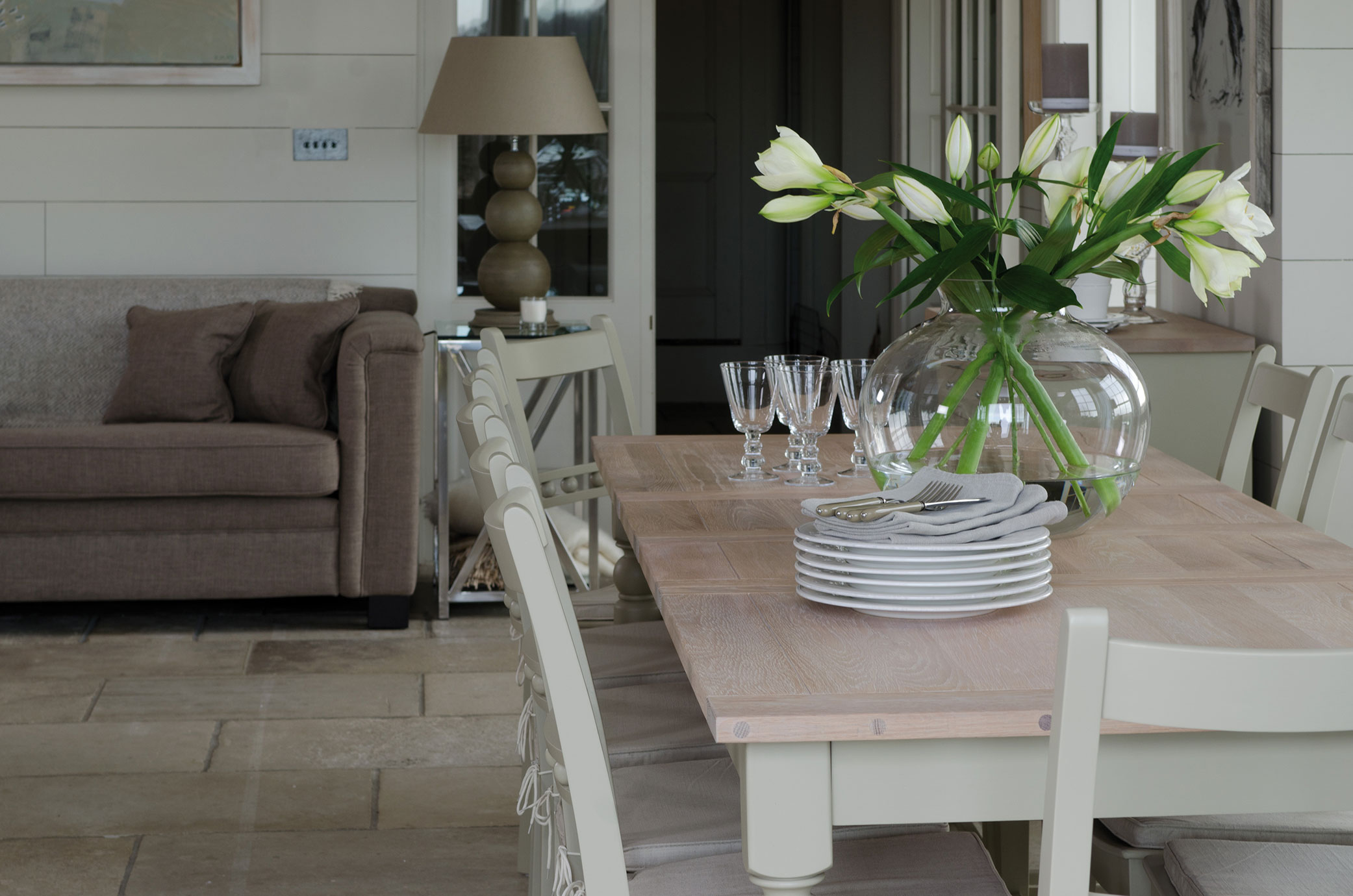 Heller, gemütlicher Wohn- und Essbereich mit modernem Sofa, stilvollem Holztisch, weißen Stühlen und großer Glasvase mit weißen Lilien