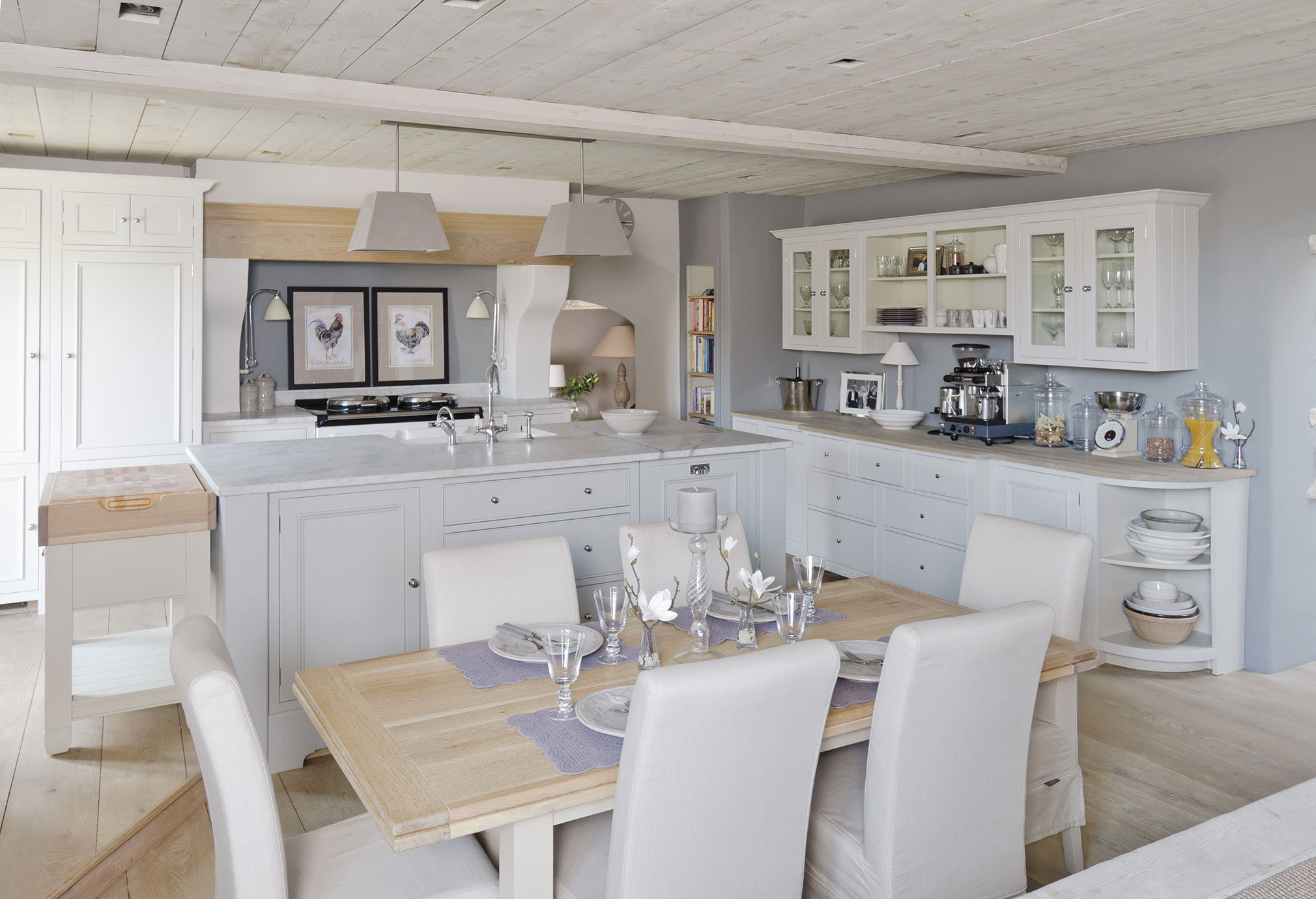 Große, helle Landhausküche mit Kücheninsel, weißem Esstisch, Glasvitrinen und moderner Ausstattung im eleganten Stil