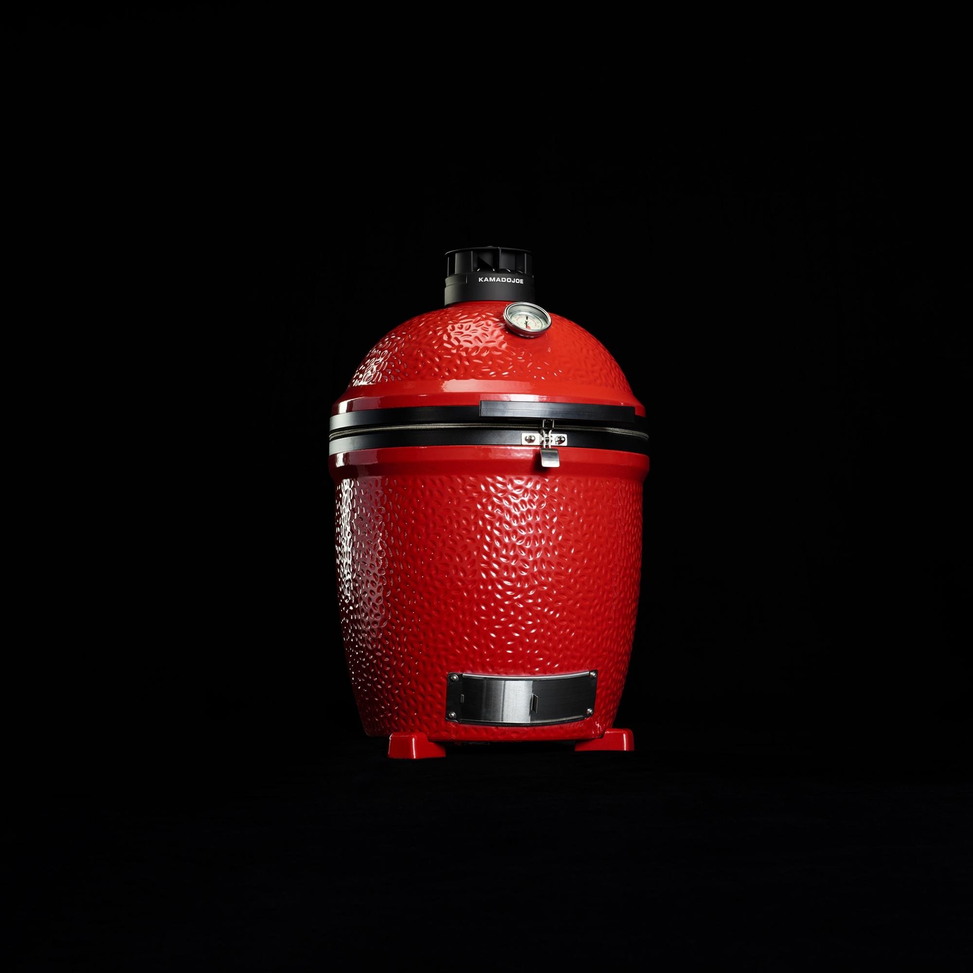 Roter Keramikgrill im Kamado-Stil mit Temperaturanzeige und Metallbeschlägen auf schwarzem Hintergrund