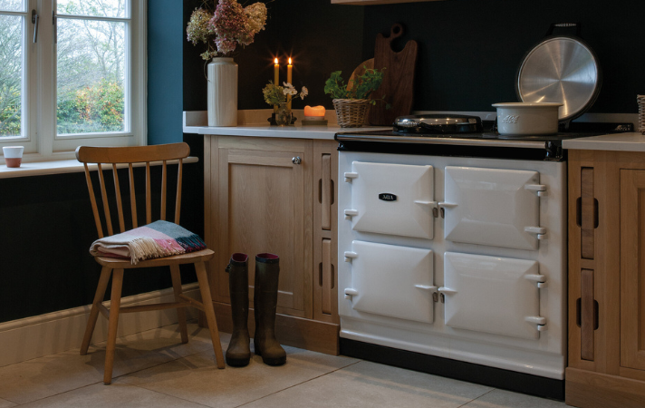 Helle Landhausküche mit AGA-Herd, Stuhl mit Decke, Gummistiefeln und dekorativen Blumenarrangements auf der Arbeitsfläche