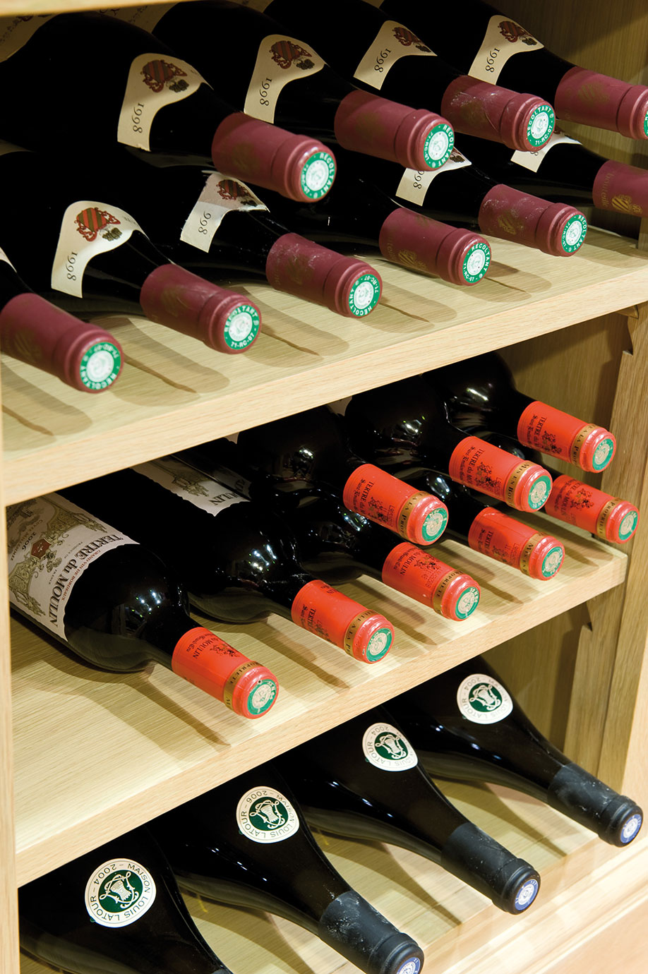 Weinregal aus Holz mit mehreren gelagerten Weinflaschen unterschiedlicher Jahrgänge und Etiketten