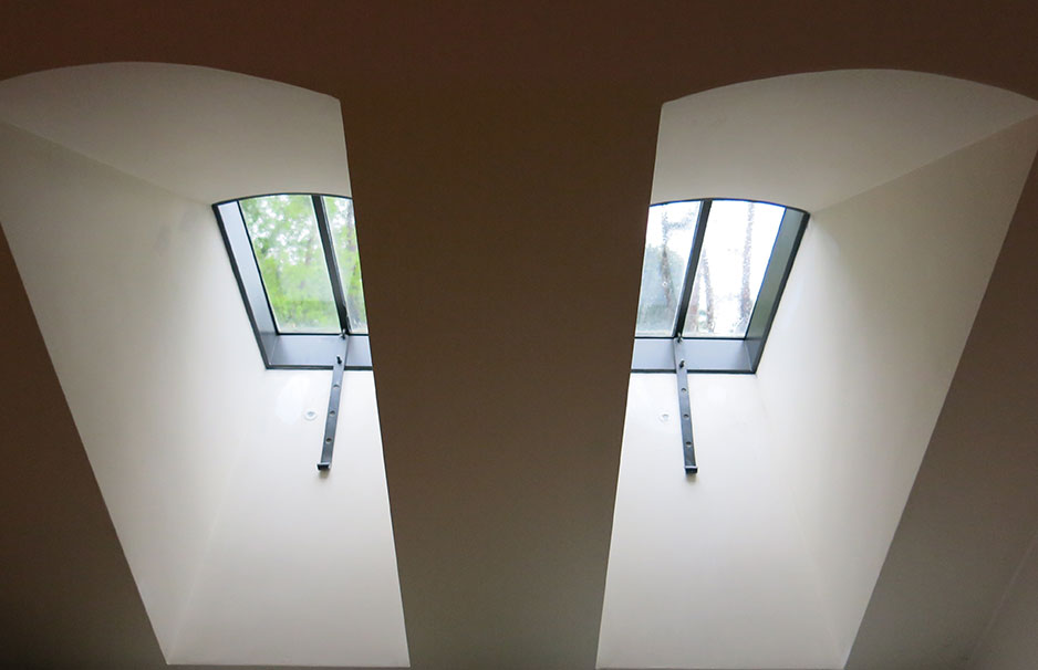 Zwei nebeneinanderliegende, rechteckige Dachflächenfenster mit Metallrahmen und Blick auf Bäume