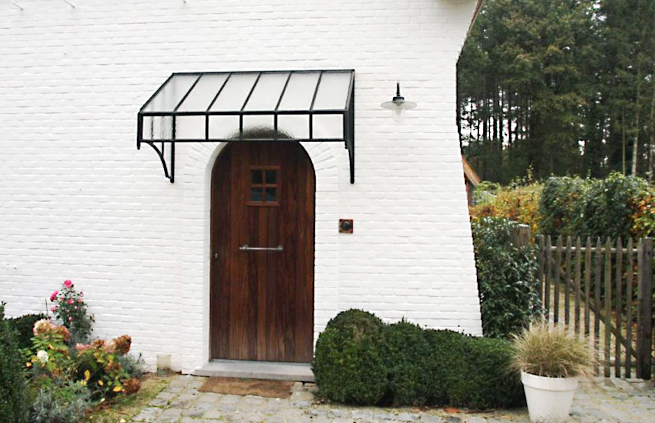 Modernes Glasvordach mit schwarzem Metallgestell über einer Holztür an einem weißen Backsteinhaus