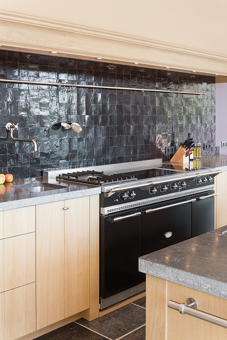 Helle, moderne Küche mit schwarzem Fliesenrückwand, großem Gasherd, Holzschränken und Küchenhelfern auf der Arbeitsplatte