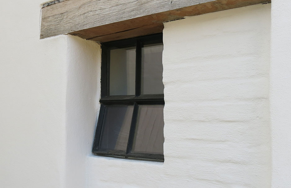 Altes Fensterelement mit schwarzem Rahmen und vier Scheiben in einer weißen Wand, unter Holzsturz, eins der Fenster geöffnet