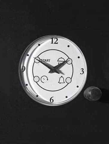 Runder mechanischer Küchentimer mit schwarzen Zahlen, Symbolen und einem Drehknopf vor schwarzem Hintergrund