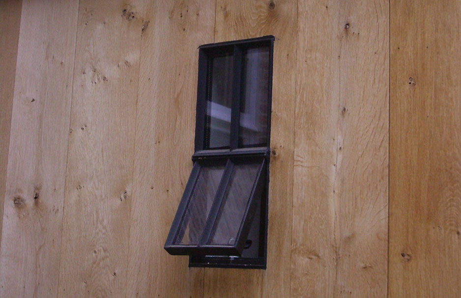Kleines, schwarzes Fenster mit Kippmechanismus eingebaut in einer Wand aus hellen Holzbrettern