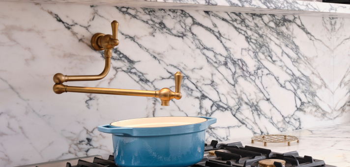 Eleganter Küchenbereich mit goldfarbenem Wasserhahn, blauem Topf und weiß-grauer Marmorwand