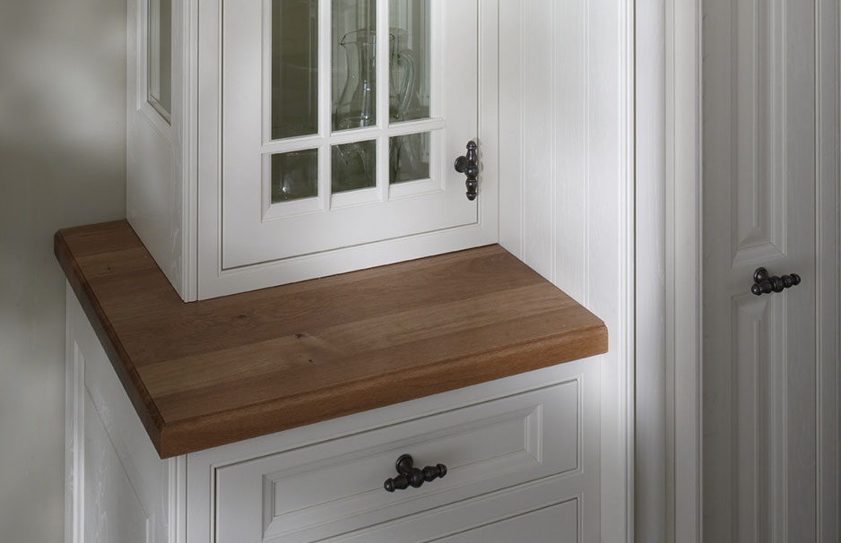 Detailaufnahme einer weißen Landhausküche mit massivem Holzboden, Vitrinenschrank mit Glastüren und dekorativen Metallgriffen