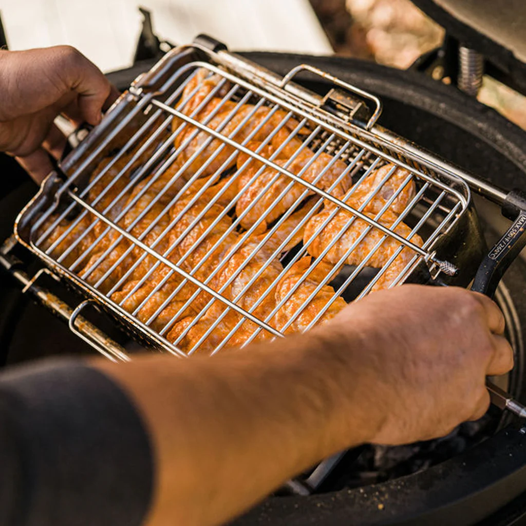 Mann hält einen Grillkorb mit mehreren Würstchen über einen runden Holzkohlegrill