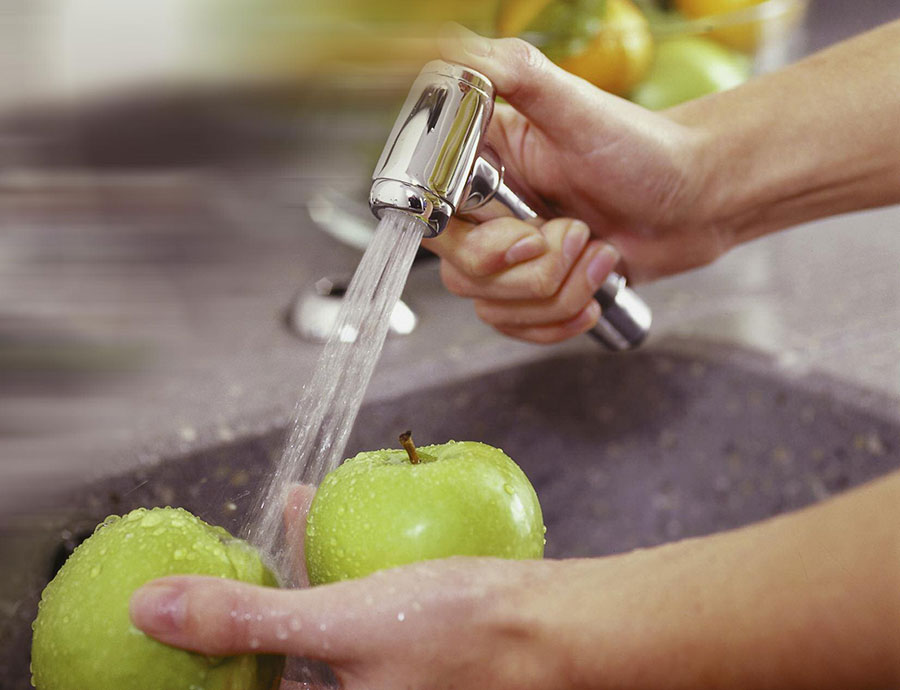 Person wäscht einen grünen Apfel unter einem Wasserhahn in der Küchenspüle