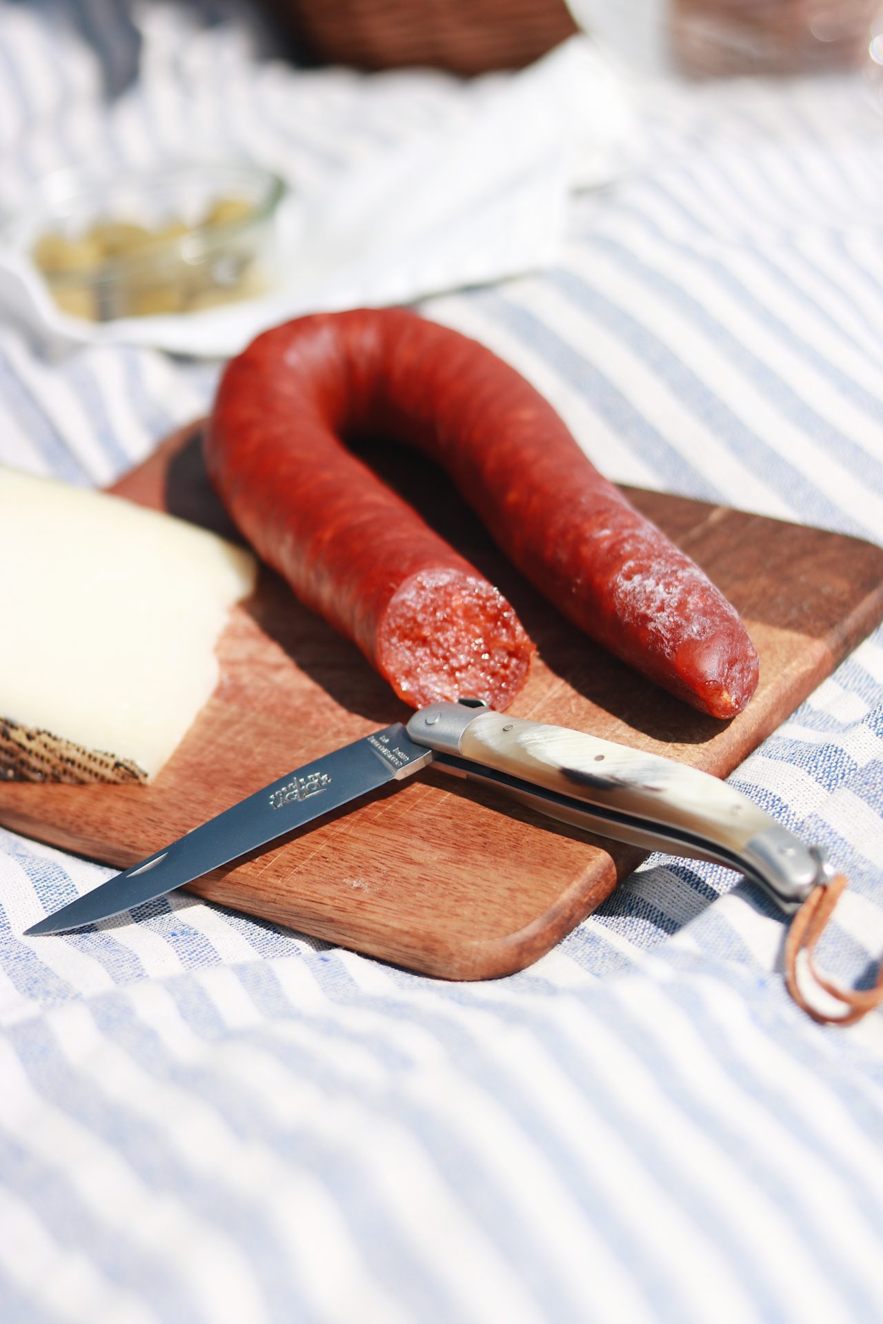 Auf einem Holzbrett liegen eine angeschnittene Salami, ein Stück Käse und ein Klappmesser – ideal für Picknick oder Brotzeit