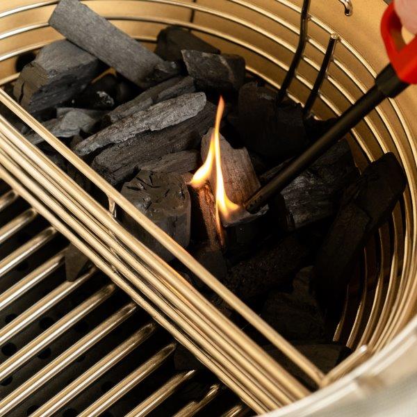 Nahaufnahme: Grillrost mit Holzkohle, die mit einem elektrischen Anzündstab entzündet wird