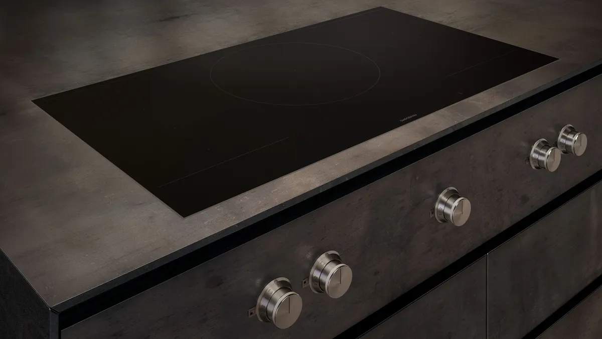 Schwarzes Induktionskochfeld mit eleganten Drehknöpfen, eingebaut in eine moderne Küchenzeile aus dunklem Material