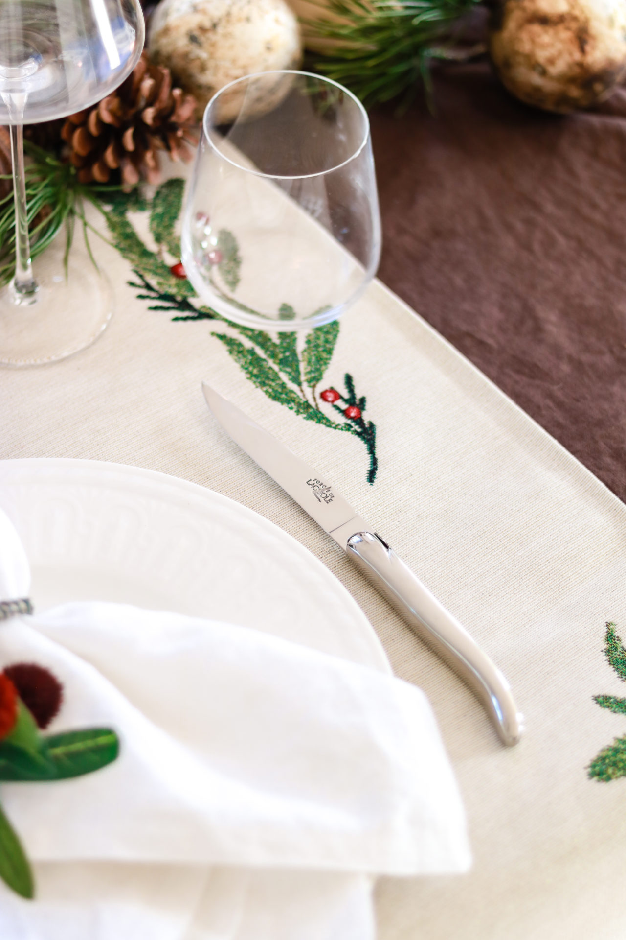 Nahaufnahme eines weihnachtlich dekorierten Tisches mit besticktem Läufer, Messer, Glas und Teller