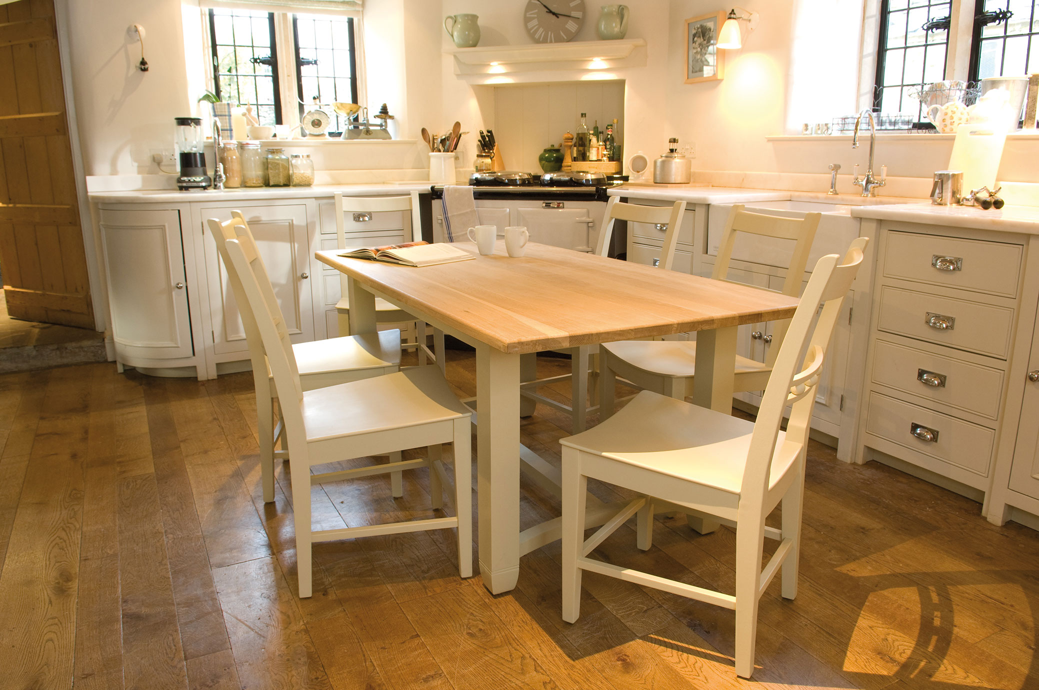 Holztisch mit vier weißen Stühlen in einer hellen, modernen Landhausküche mit Holzfußboden und Küchenzeile im Hintergrund