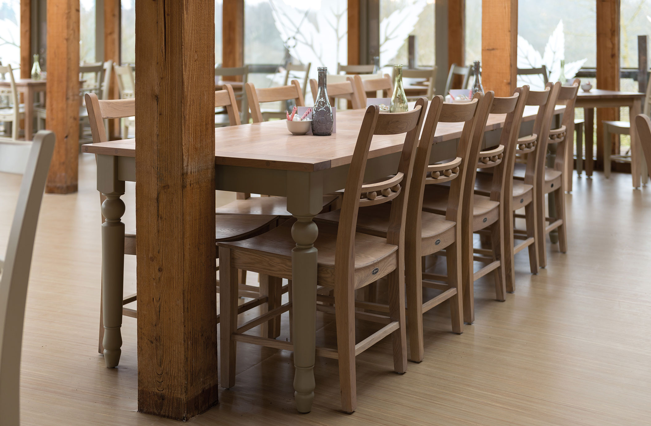 Langer Holztisch mit Holzstühlen in einem lichtdurchfluteten Restaurant mit natürlicher Einrichtung