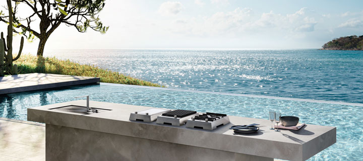 Elegante Außenküche mit Kochfeld, Spüle und Meerblick, am Rand eines Infinity-Pools aufgestellt