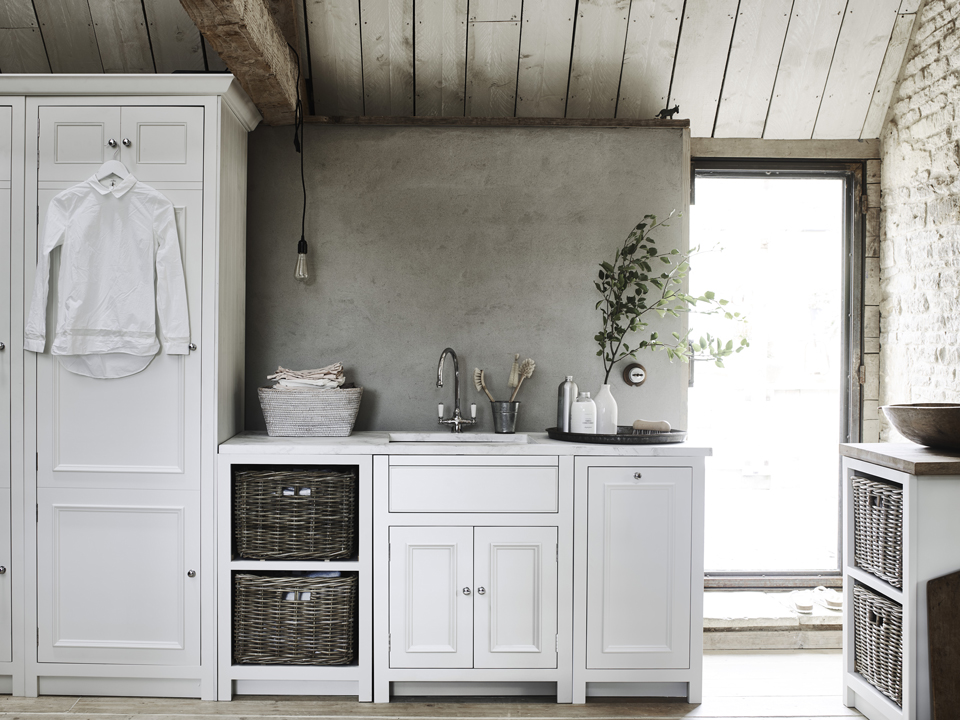 Gemütliche Küche im Landhausstil mit weißen Schränken, Spüle, Wandregal, Körben und aufgeräumter Dekoration, natürliche Materialien und viel Licht