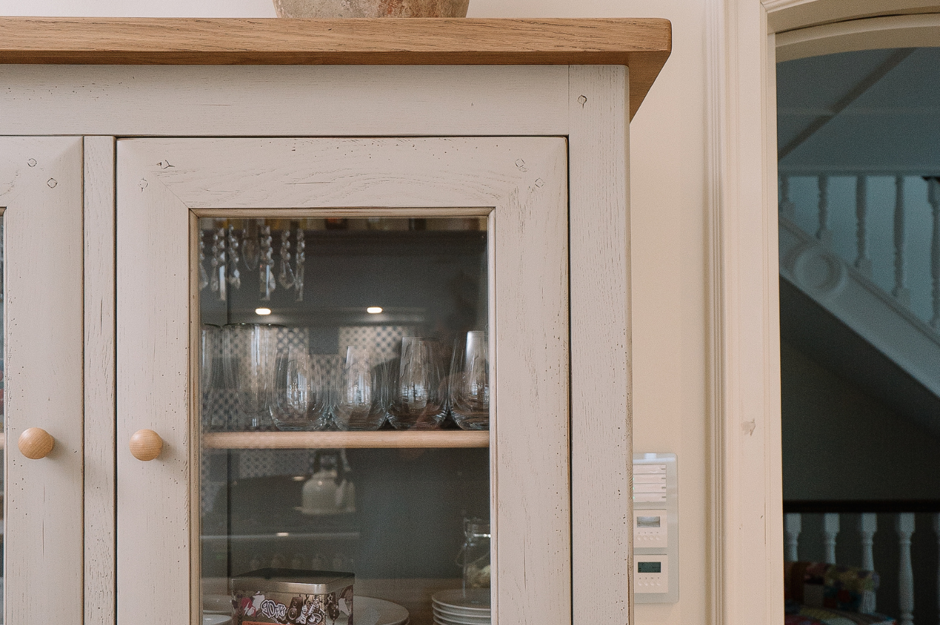 Weißer Vitrinenschrank im Landhausstil mit Glastüren, darin Gläser und Geschirr, Holzplatte oben