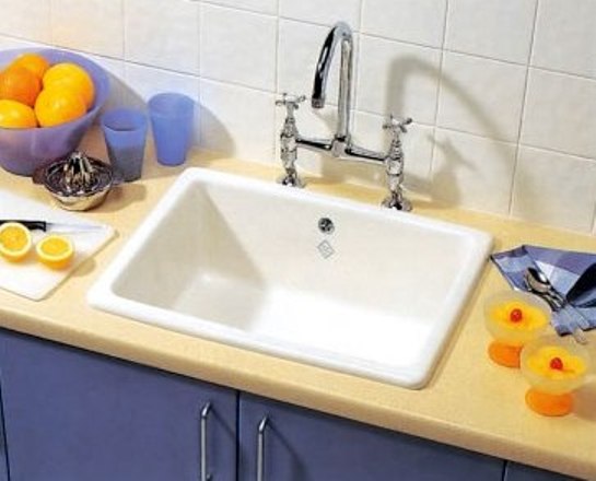 Weiße Keramik-Küchenspüle auf beiger Arbeitsplatte mit Doppelarmatur, umgeben von Orangen, Gläsern, Zitronenhälften und Küchenutensilien