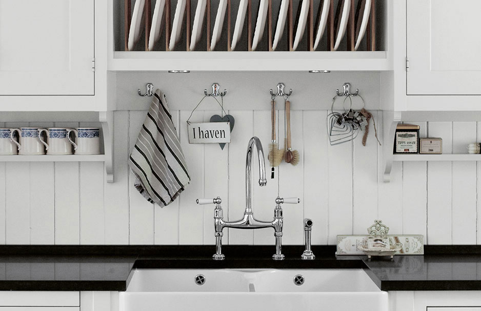 Helle Küche im Landhausstil mit weißem Spülbecken, Hakenleiste mit Küchenutensilien, Tassenregal und geöffnetem Geschirrfach mit Tellern.