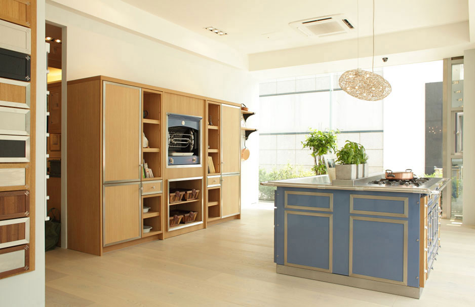 Helle, moderne Küche mit blauer Kochinsel, eingebauten Holzschränken, viel Tageslicht und Pflanzen auf der Arbeitsfläche