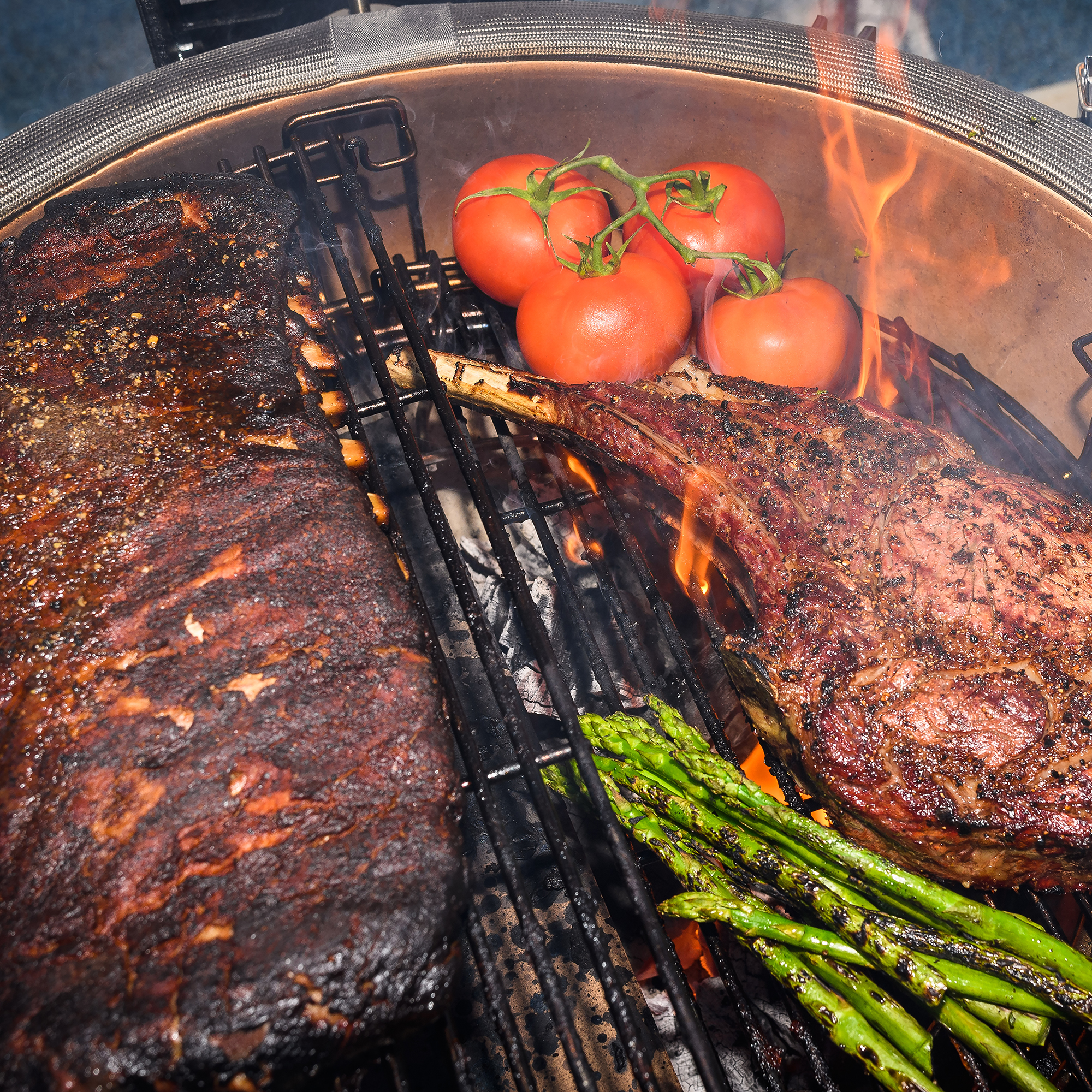 Großaufnahme von gegrilltem Tomahawk-Steak, Rinderbraten, grünem Spargel und Tomaten auf einem Grill