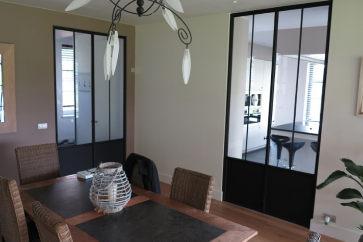 Modern eingerichtetes Esszimmer mit dunklen Glastüren, Holztisch und geflochtenen Stühlen