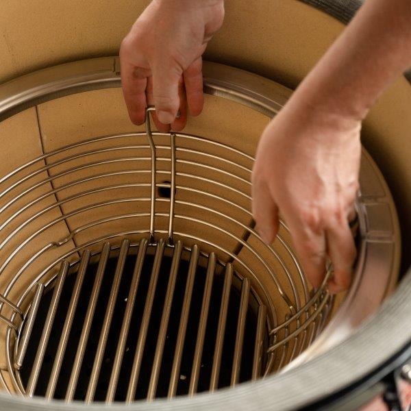 Person setzt einen runden Edelstahlkohlekorb in einen Kamado Keramikgrill ein