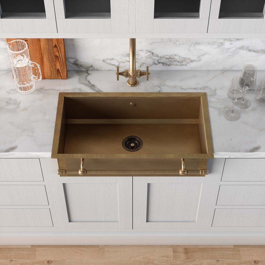 Goldene Küchenspüle mit eleganter Armatur auf einer Arbeitsplatte aus weißem Marmor, Gläser und Krug im Hintergrund