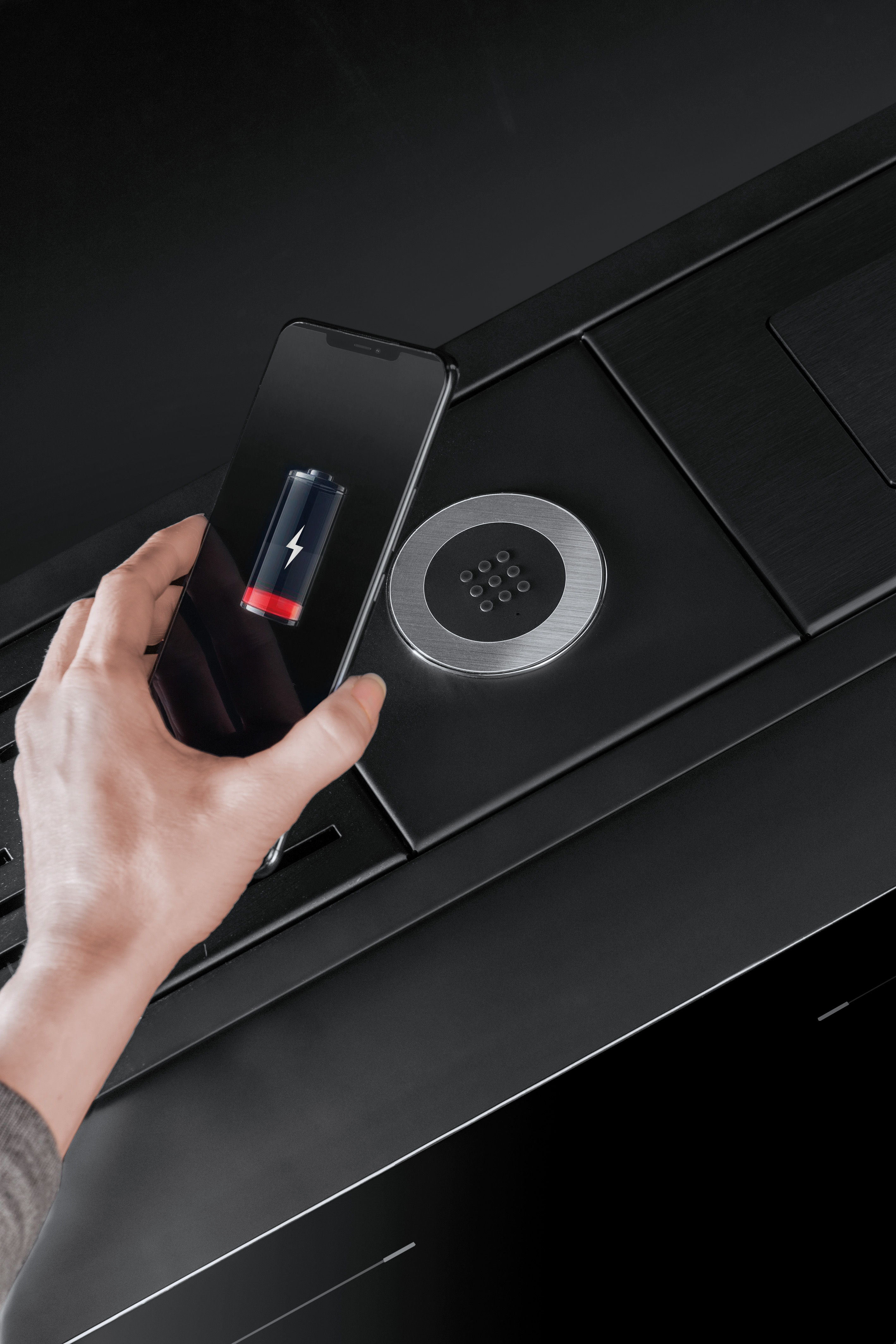 Hand hält ein Smartphone mit niedrigem Akkustand über eine kabellose Qi-Ladestation auf einem schwarzen Tisch